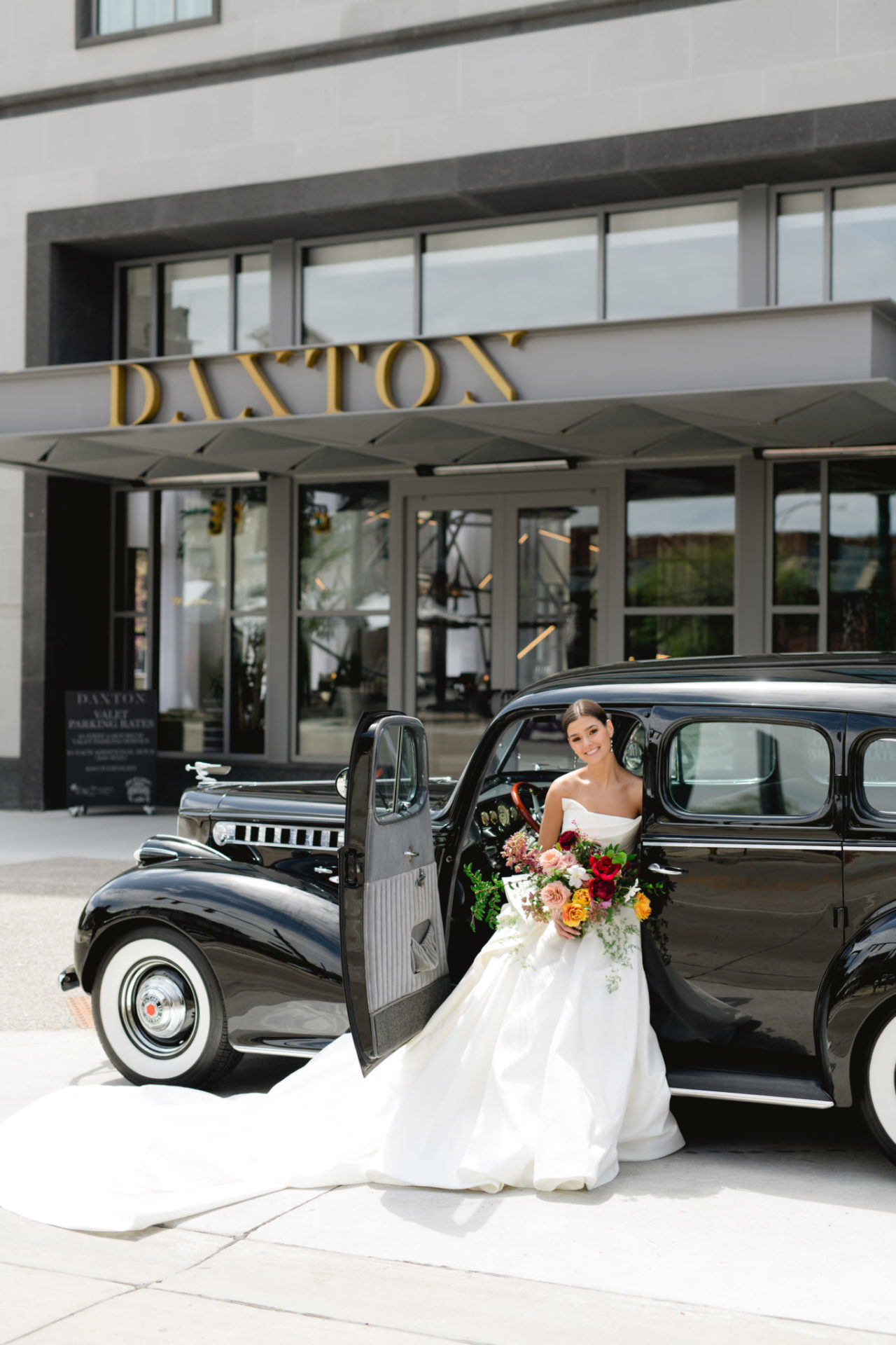 Stunning bride standing outside the Front of the Daxton Hotel in an old black car